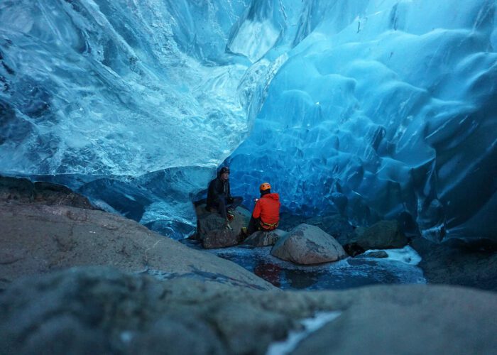 A guest chatting with their expert ice cave and glacier guide about the formation of the ice cave their sitting in on a full day glacier exploration hiking tour.